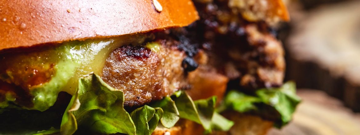 Side view of a cheeseburger with a grilled beef patty, melted cheese, fresh lettuce, and soft burger buns.
