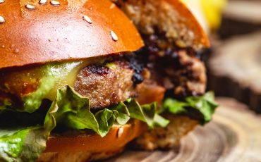 Side view of a cheeseburger with a grilled beef patty, melted cheese, fresh lettuce, and soft burger buns.